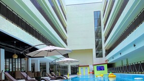 Una piscina interior con sillones de descanso y sombrillas, rodeada por un edificio de varios pisos con balcones.