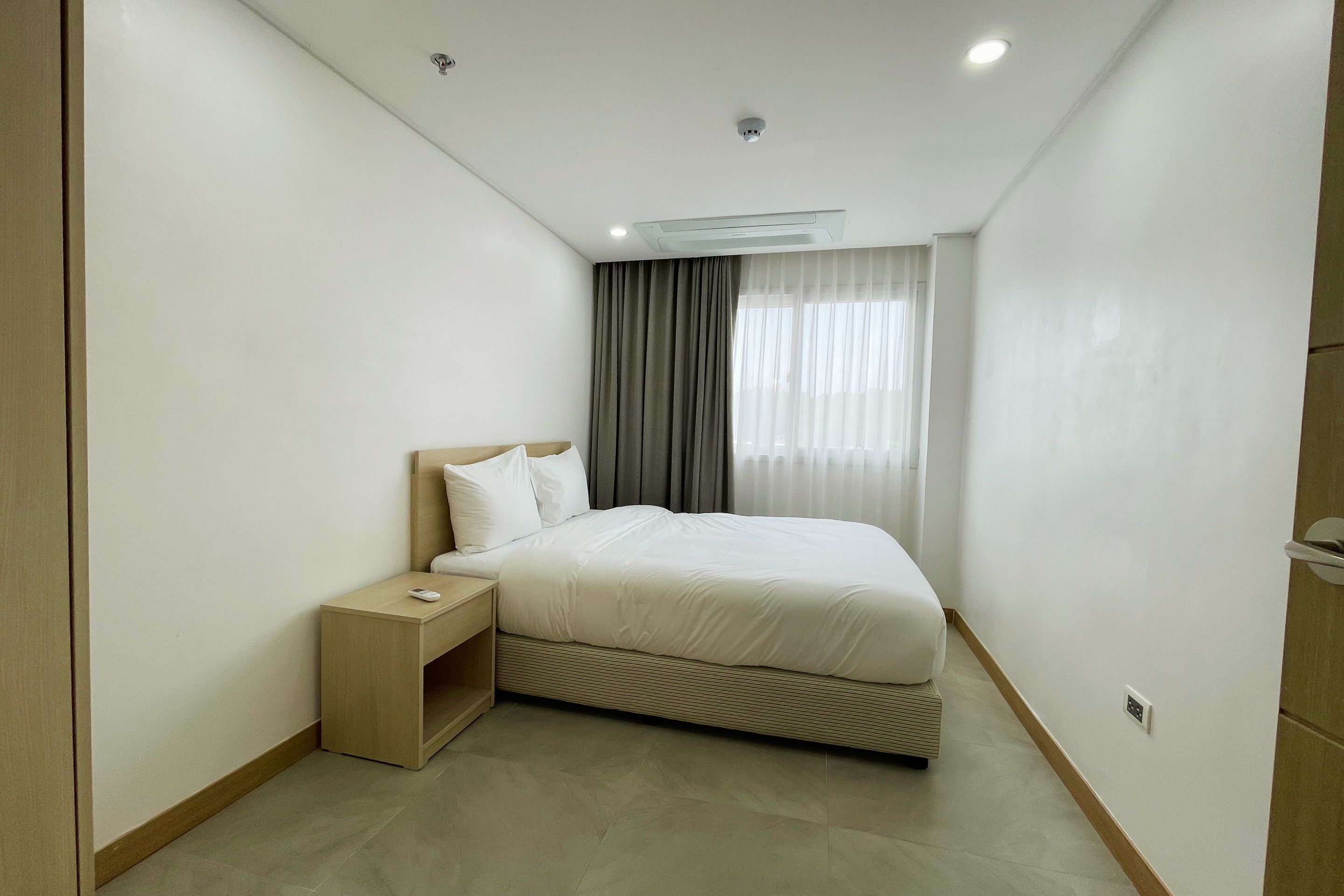 Habitación de hotel moderna con una cama individual, una mesita de noche y un ventanal con cortinas.