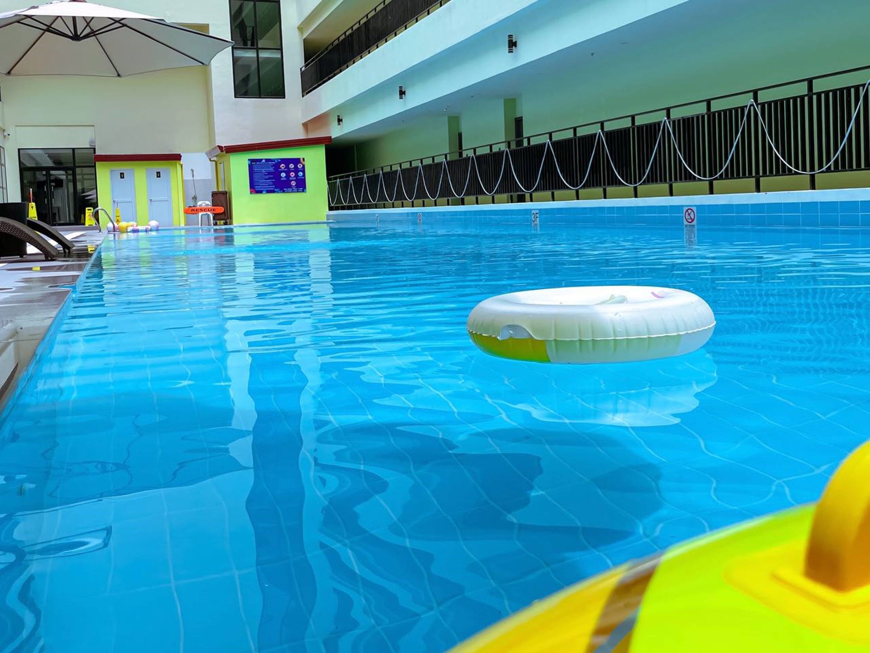 An indoor swimming pool with clear blue water, a floating ring, and a safety sign.