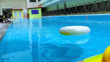 An indoor swimming pool with clear blue water, a floating ring, and a safety sign.