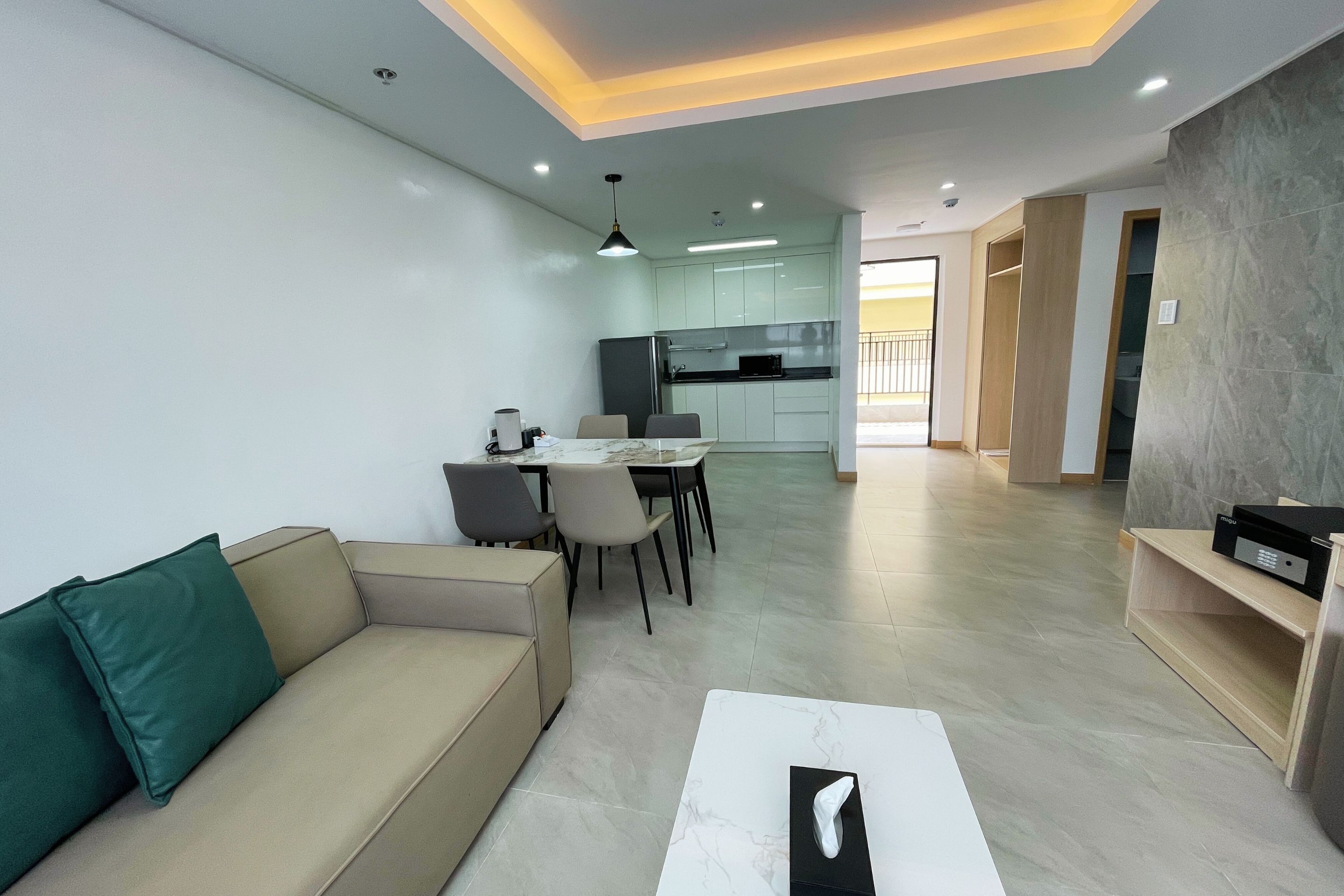 A modern living room with a beige sofa, a dining area with a table and chairs, and a kitchen in the background.
