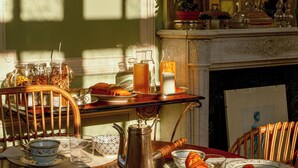 Une table à manger dressée avec différents plats, une cafetière et un panier de pain.