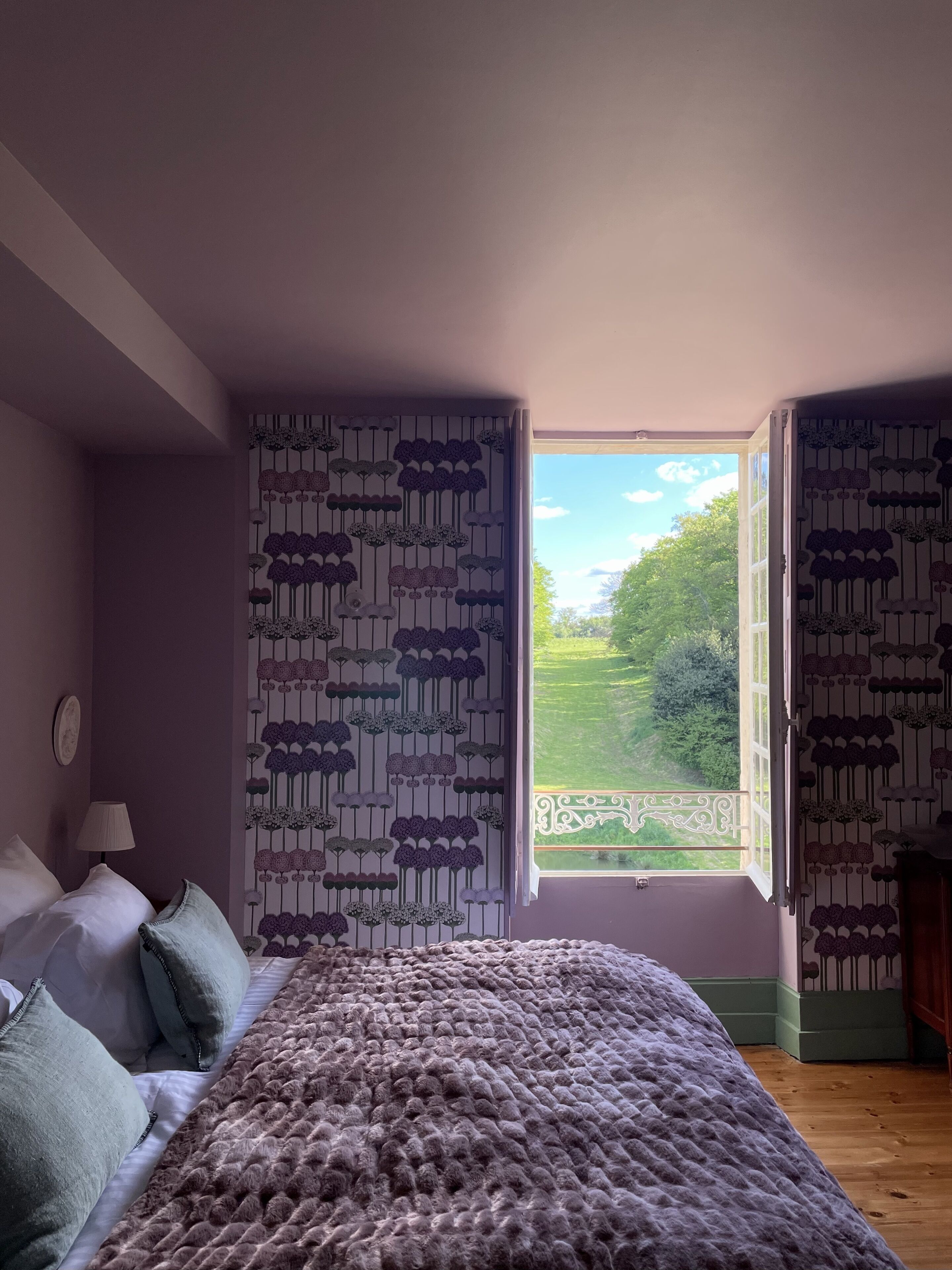 Quarto com uma cama grande, janela com cortinas e vista para uma paisagem verde.
