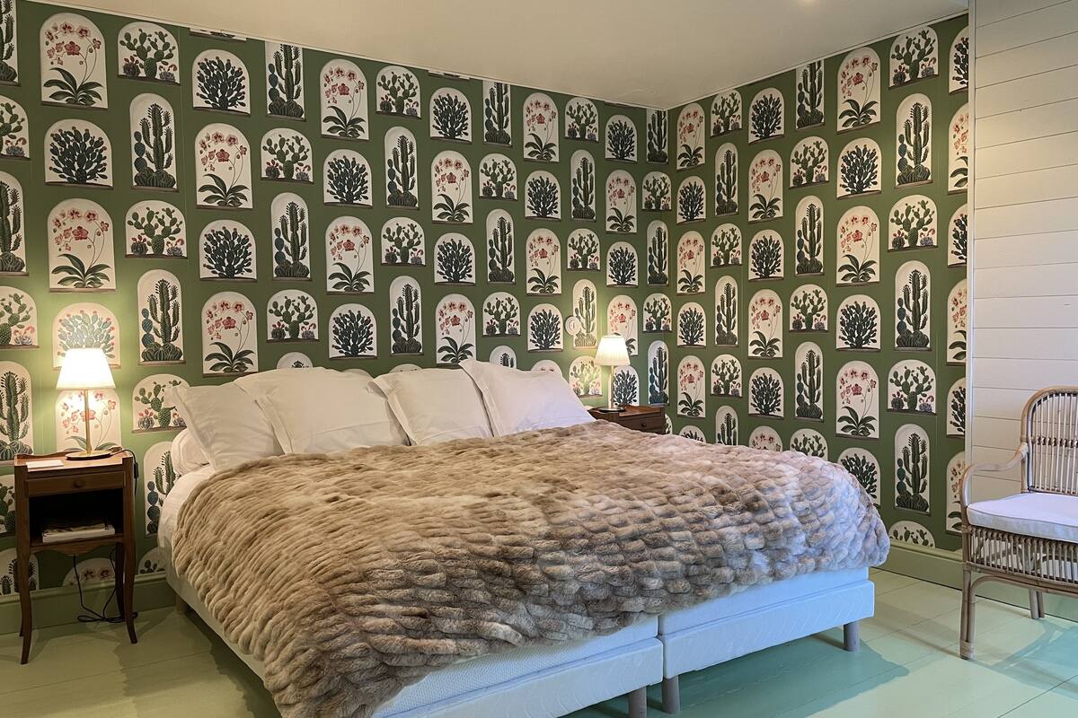 Une chambre à coucher comprenant un lit, une table de chevet, une chaise et un mur orné d’un motif de cactus.