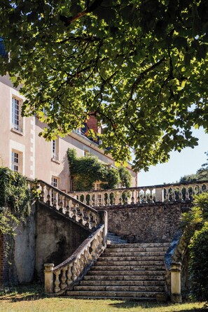 Un escalier en pierre menant à un bâtiment doté d’un balcon, le tout entouré de verdure.