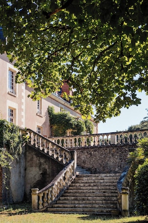 A stone staircase leading to a building with a balcony, surrounded by greenery.