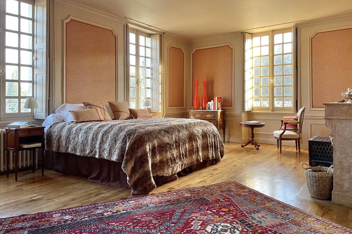 Une chambre spacieuse avec un grand lit, de nombreuses fenêtres, un plancher en bois et un décor traditionnel.