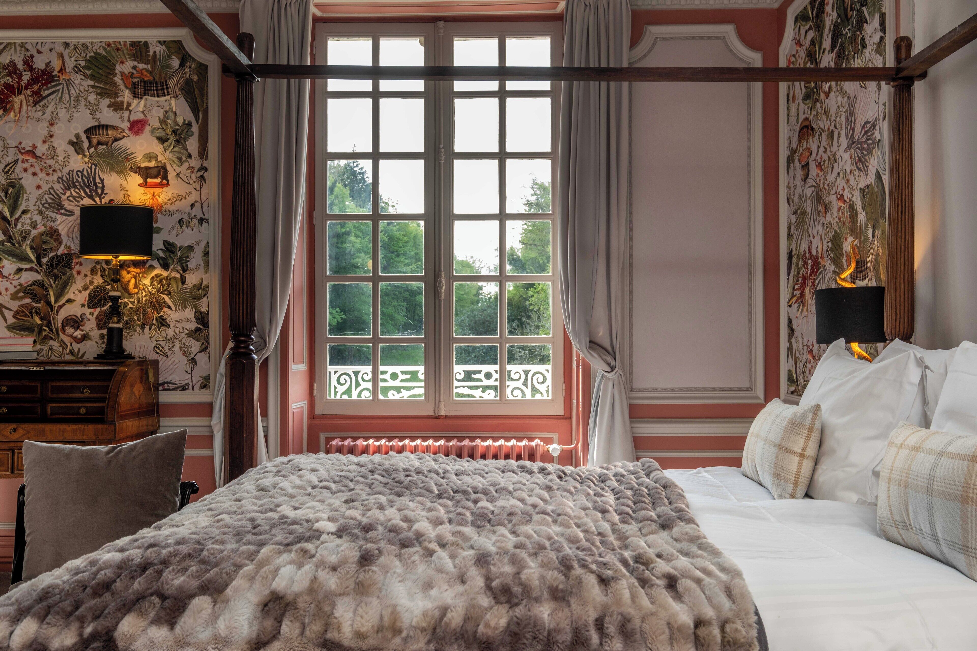 A bedroom with a large bed, a window with a view, a radiator, and a lamp on a nightstand.