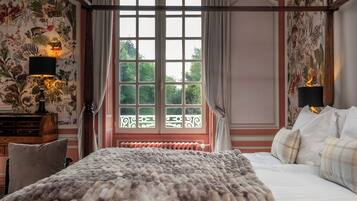 A bedroom with a large bed, a window with a view, a radiator, and a lamp on a nightstand.
