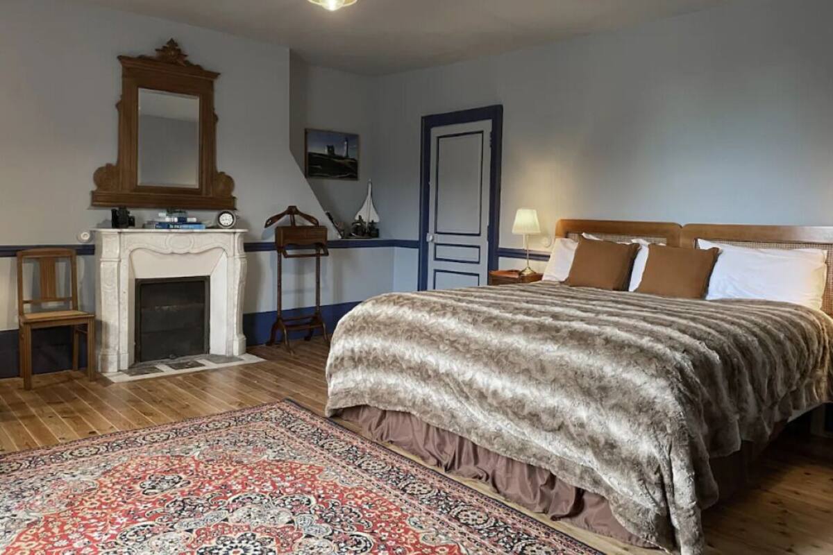 Une chambre à coucher avec un grand lit, une cheminée, une chaise en bois, un bureau et un miroir.