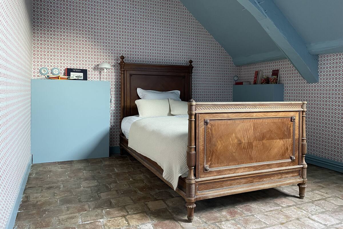 Une chambre à coucher avec un lit en bois, une armoire bleue, un papier peint à motifs et un plafond en pente.