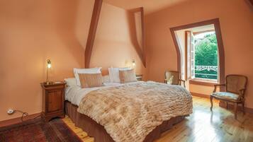 A bedroom with a large bed, a nightstand, a chair, and a window with a view of greenery.