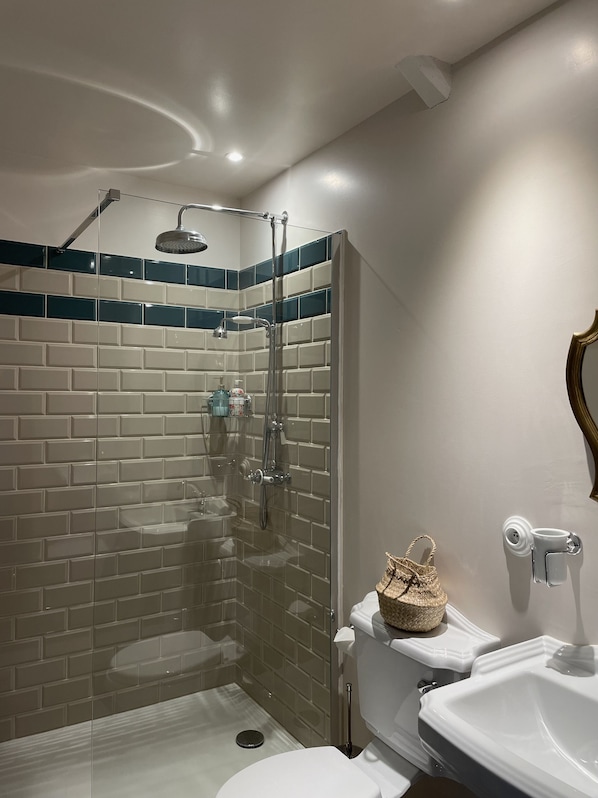 Een moderne badkamer met een glazen douchecabine, witte tegels en een witte wastafel.
