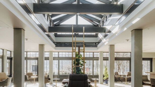 Een ruime lobby met een hoge plafond, grote ramen en een centraal zitgedeelte met twee stoelen en een tafel.