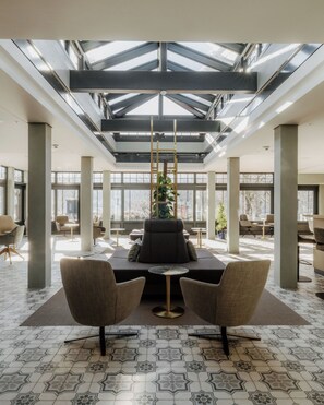 A spacious lobby with a high ceiling, large windows, and a central seating area with two chairs and a table. - Hotel Auerhahn (Schluchsee)