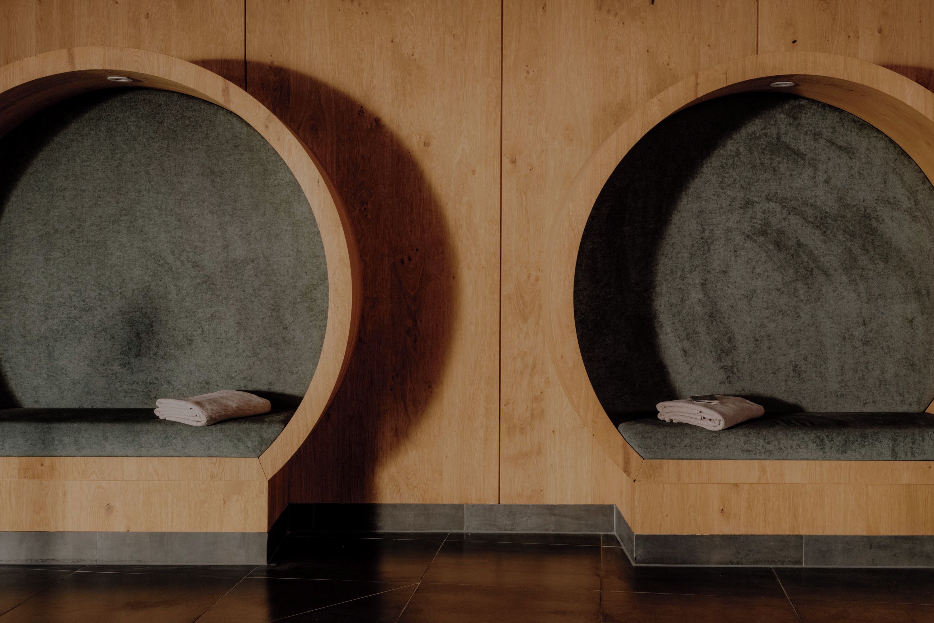 Deux espaces de détente en bois, en forme d’arche, avec des coussins gris et des serviettes pliées.