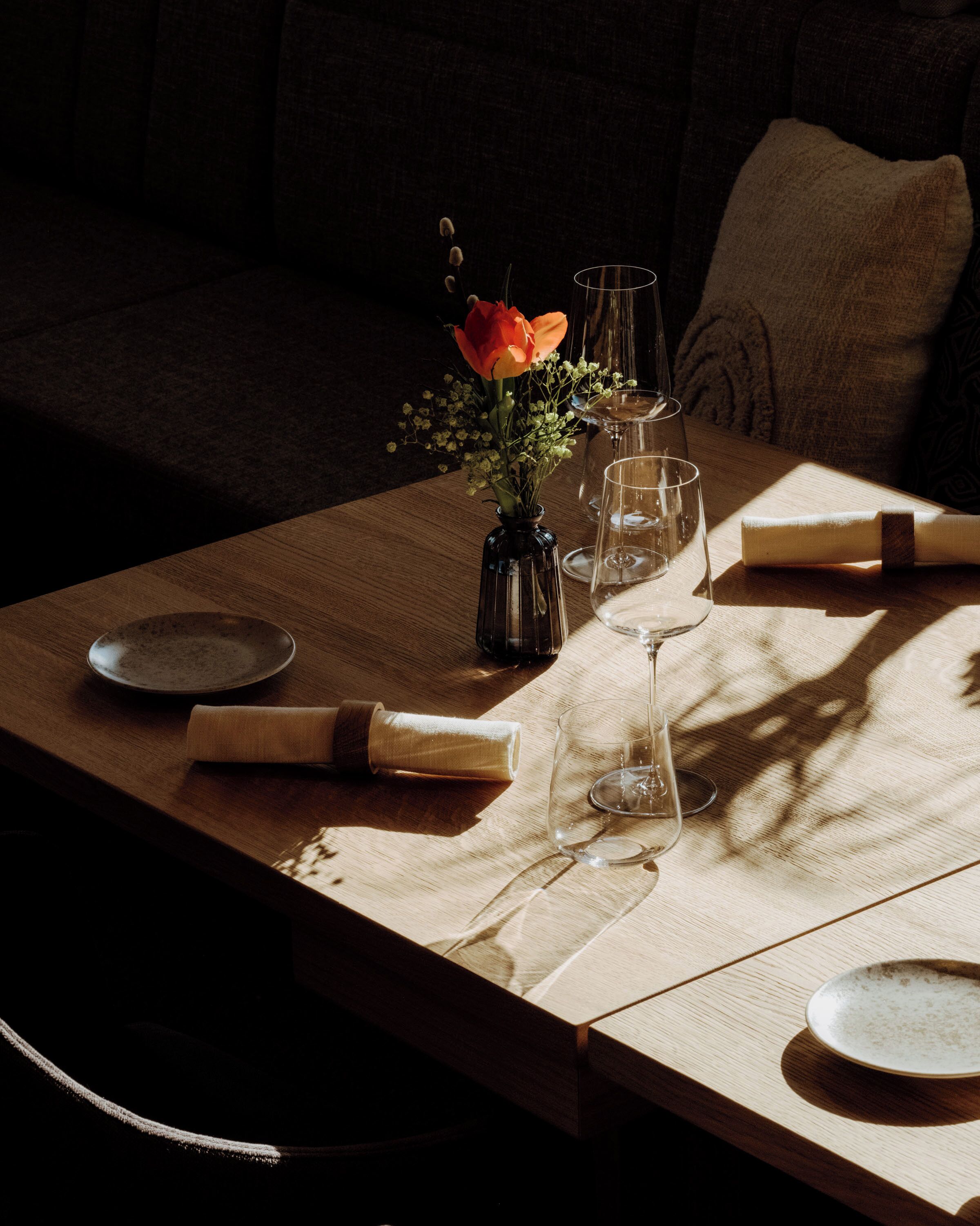 A dining table set with plates, a vase with flowers, and wine glasses.