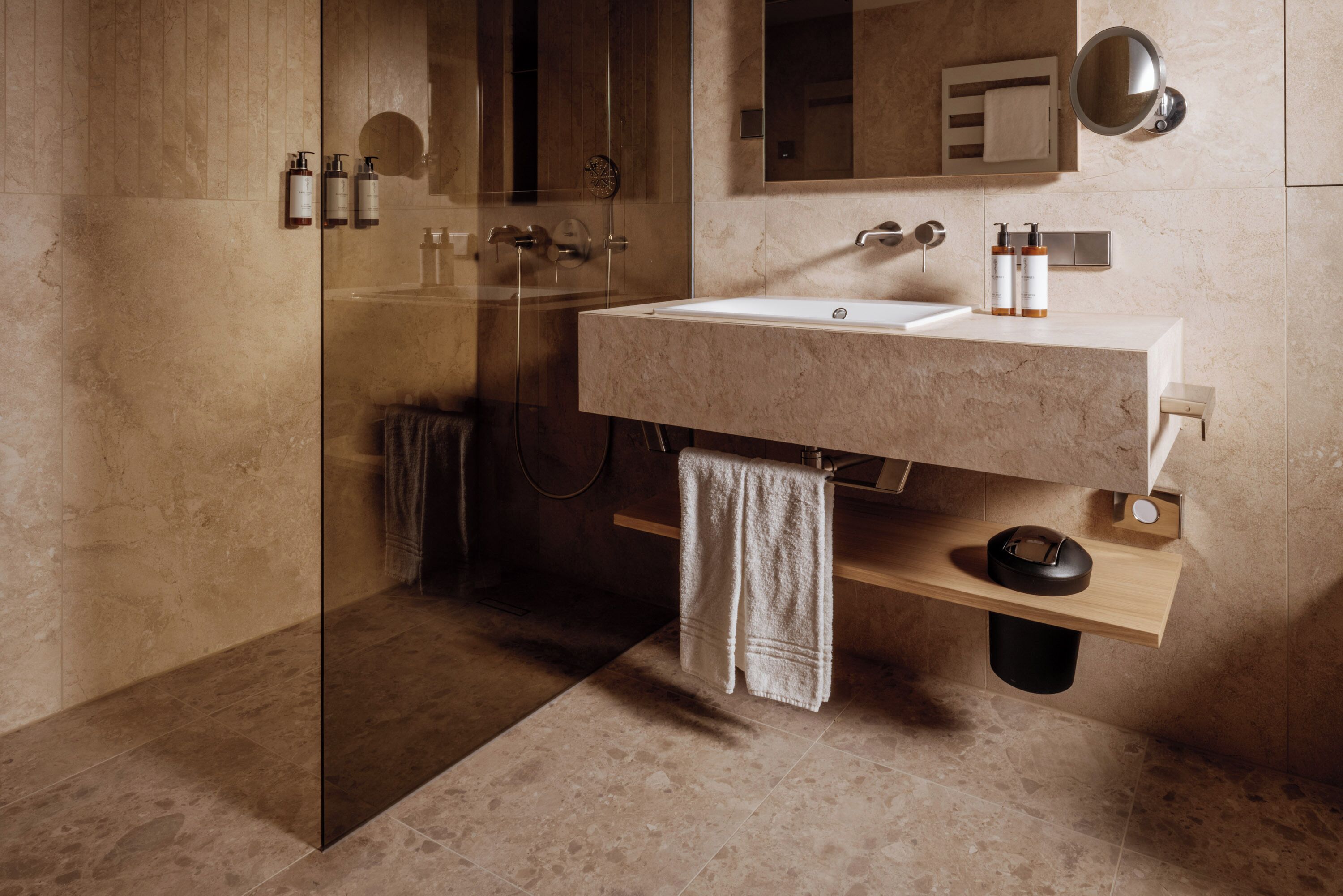 Un baño moderno con cabina de ducha de vidrio, lavamanos de mármol y estante de madera.