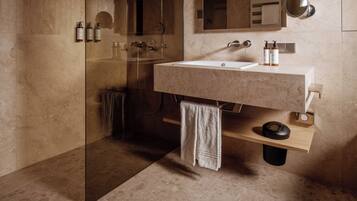Un baño moderno con cabina de ducha de vidrio, lavamanos de mármol y estante de madera.