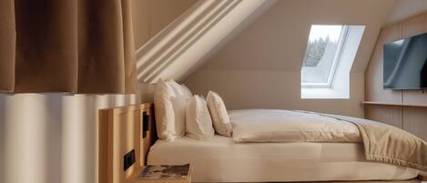 A bedroom with a bed, a bedside table, a TV, and a skylight.