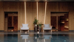 Een moderne lobby met houten paneelwanden, twee witte fauteuils en een groot reflecterend zwembad.