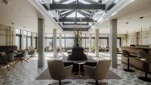 Een ruime lobby met een hoge plafond, grote ramen en een centraal zitgedeelte met een plant.