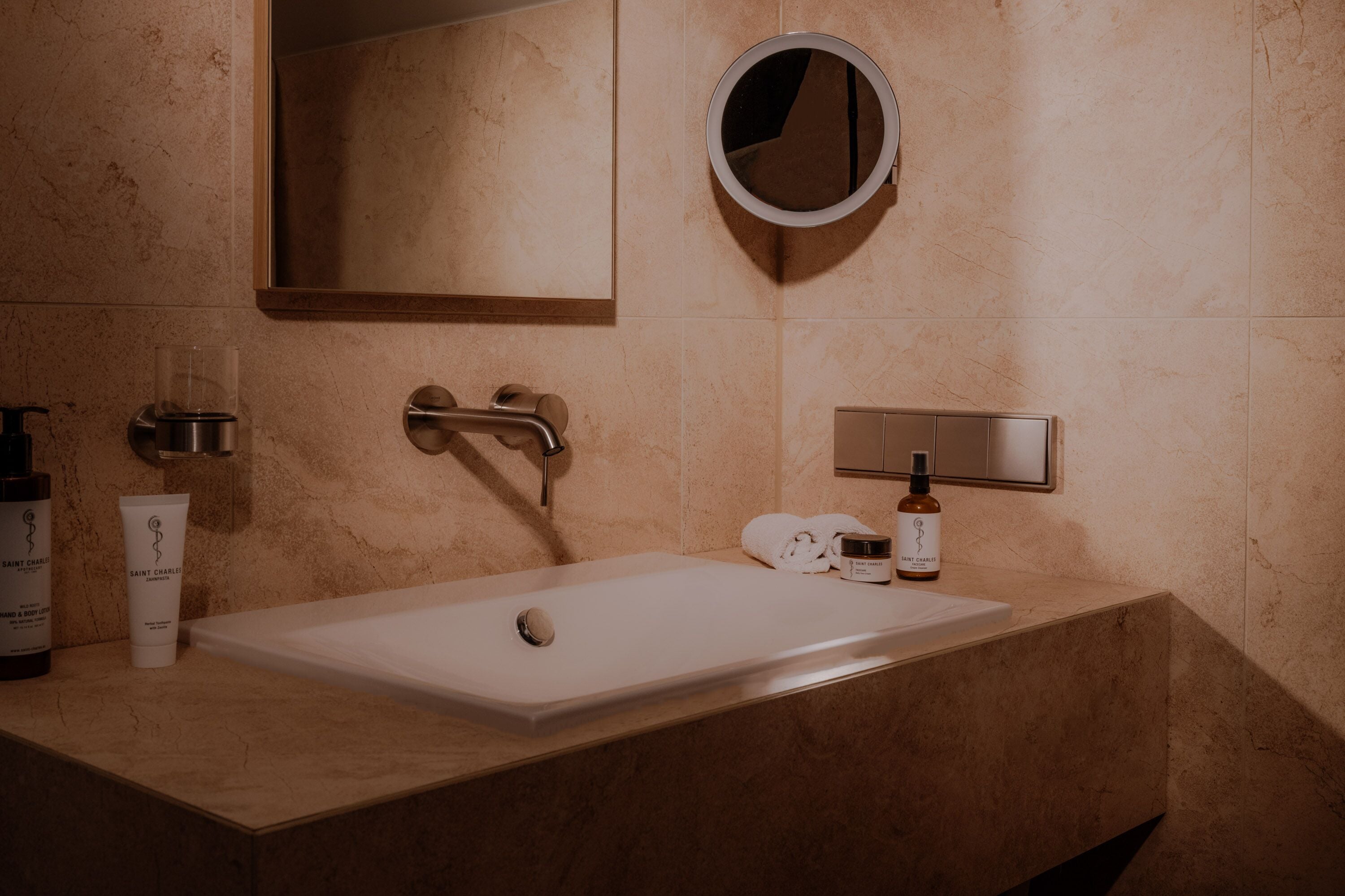 Een badkamer met een wit wastafel, een ronde spiegel en toiletartikelen op het aanrecht.