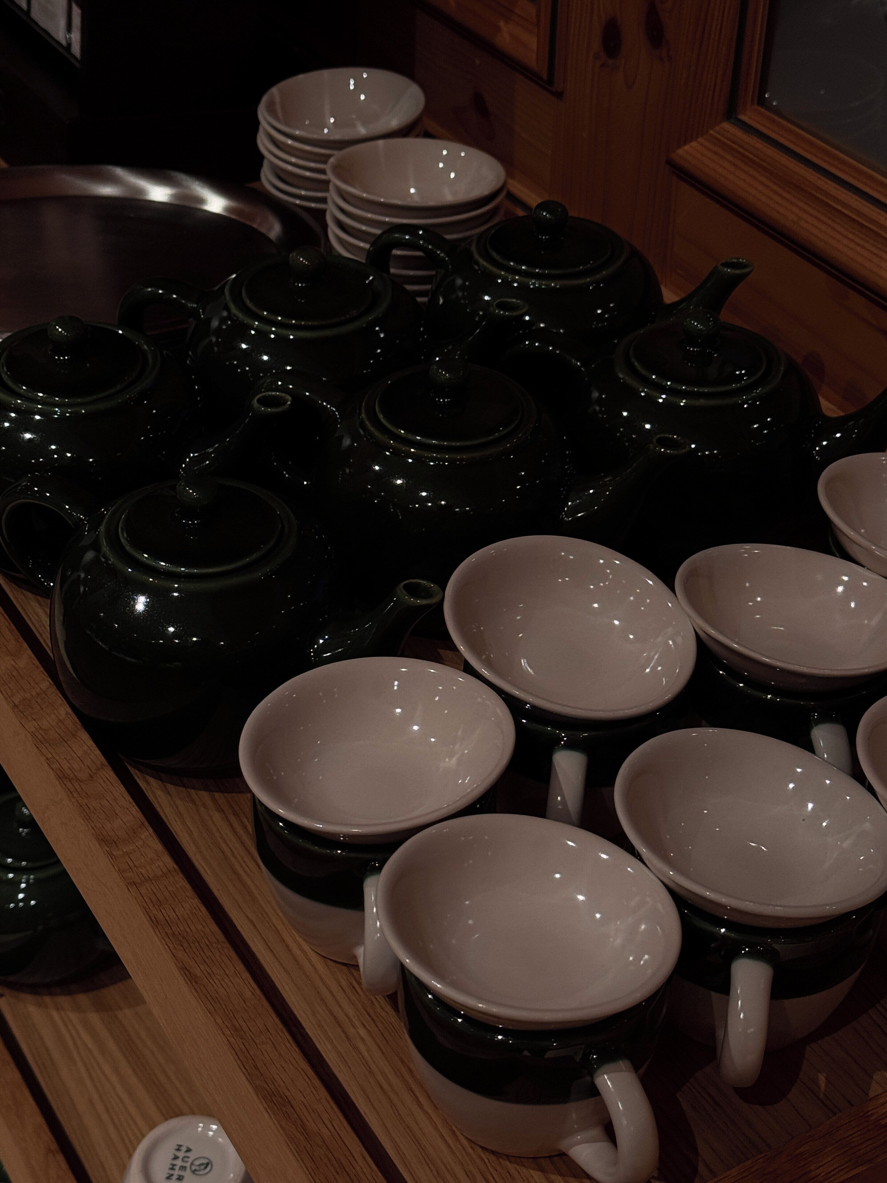 Una zona de cocina con varias teteras y tazas blancas y negras dispuestas sobre una encimera de madera.