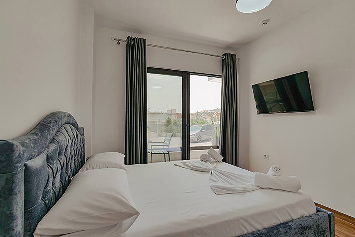 A hotel room with a bed, a TV mounted on the wall, and a window with curtains.