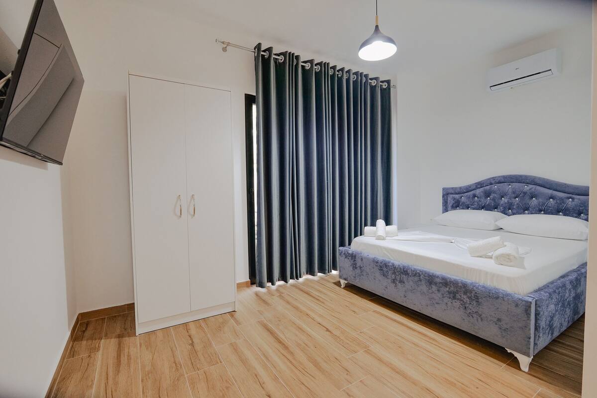 A bedroom with a bed, a wardrobe, a curtain, and an air conditioning unit.