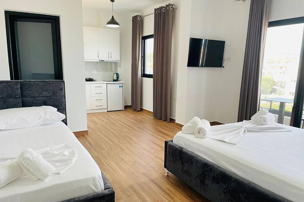 A hotel room with two beds, a kitchenette, a TV, and a view of the outdoors.