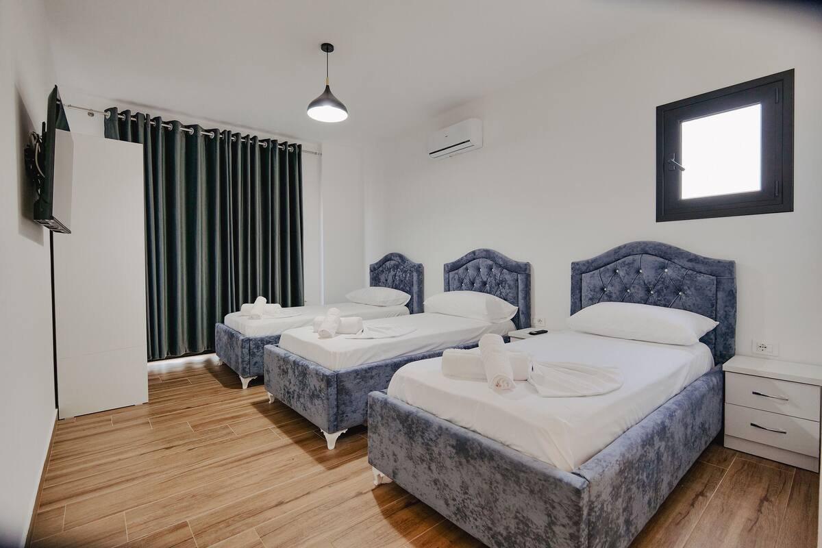 A hotel room with two beds, a ceiling light, an air conditioning unit, and a window with curtains.