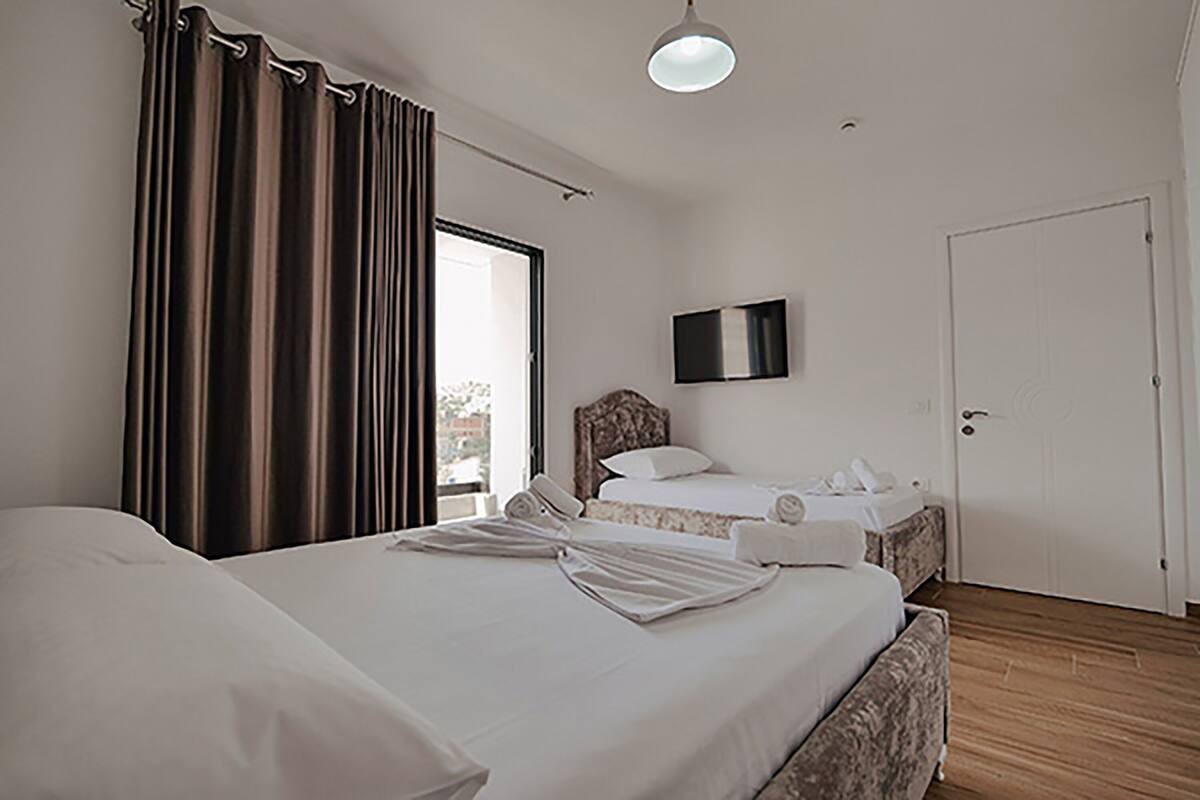 A hotel room with two beds, a flat-screen TV mounted on the wall, and a door to the right.