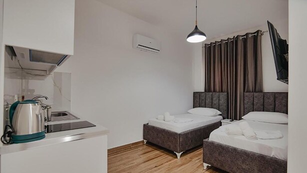 A modern hotel room with a kitchenette, two single beds, a flat-screen TV, and a large window with curtains. - Vila Muka (Ksamil)