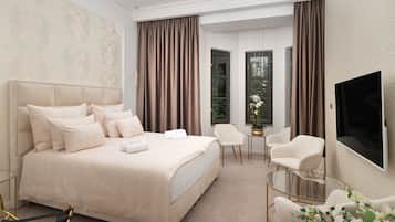 Ein Hotelzimmer mit einem großen Bett, zwei Sesseln, einem kleinen Tisch, einem Fernseher und einem Fenster mit Vorhängen.