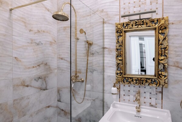 A bathroom with a shower, a sink, and a mirror with an ornate frame.