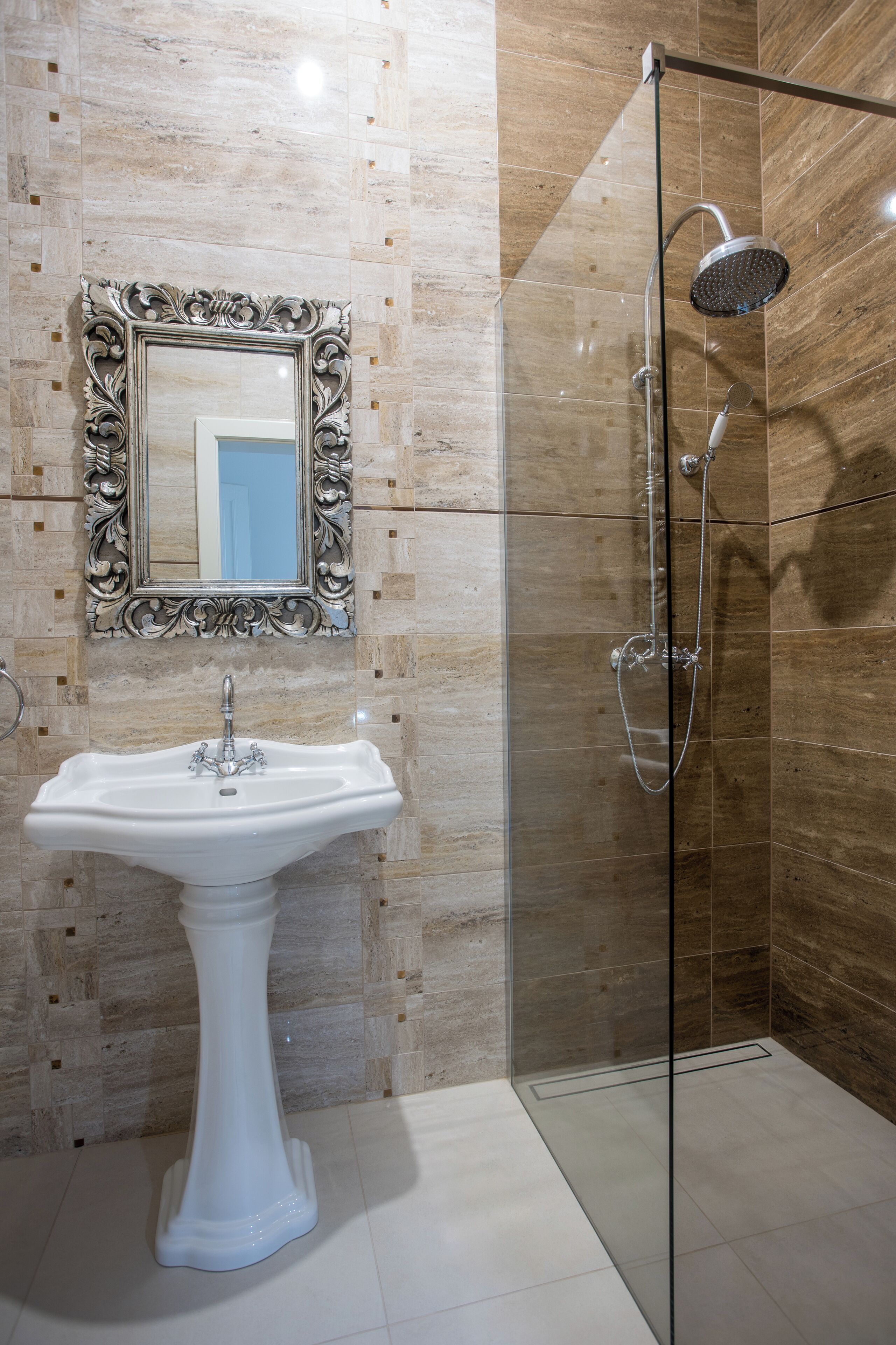 A bathroom with a pedestal sink, a shower with a glass door, and a mirror with an ornate frame.