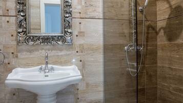 A bathroom with a pedestal sink, a shower with a glass door, and a mirror with an ornate frame.