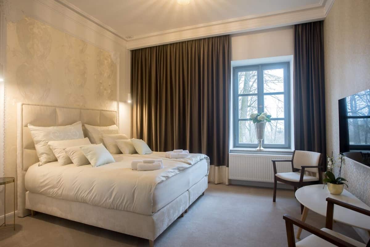 Een slaapkamer met een groot bed, een raam met gordijnen, een stoel en een tafel.