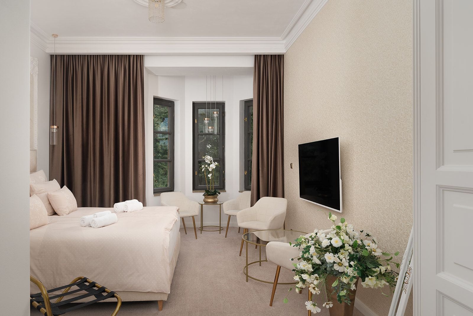 Ett hotellrum med en säng, två stolar, ett litet bord, en tv och ett fönster med gardiner.