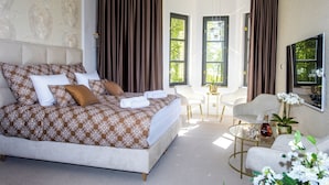 Een moderne slaapkamer met een groot bed, een glazen bijzettafeltje en een zithoek met een witte stoel en een bank.