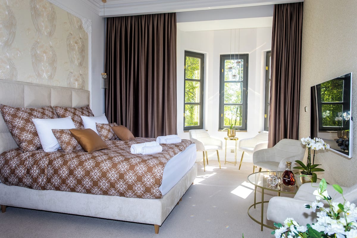Een moderne slaapkamer met een groot bed, een glazen bijzettafeltje en een zithoek met een witte stoel en een bank.