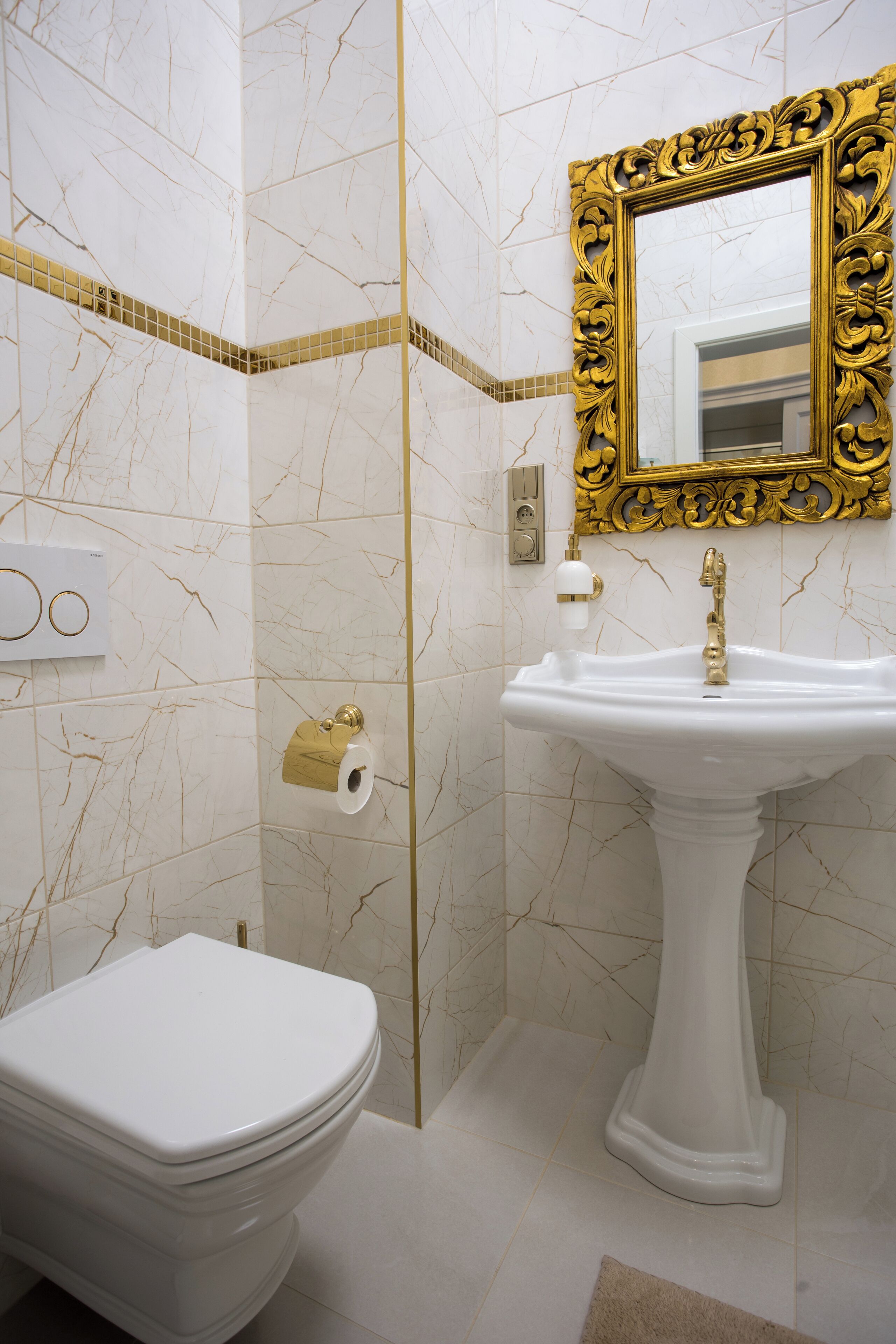 A bathroom with a white toilet, a pedestal sink, and a gold-framed mirror.