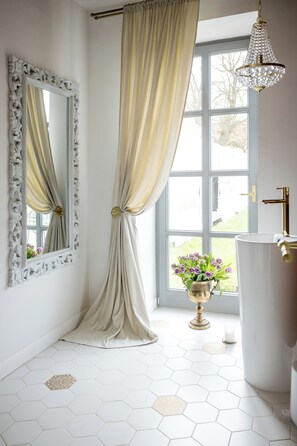 A bathroom with a large window, a white sink with gold fixtures, and a mirror with an ornate frame. - Zámek Kvasetice (Kvetinov)