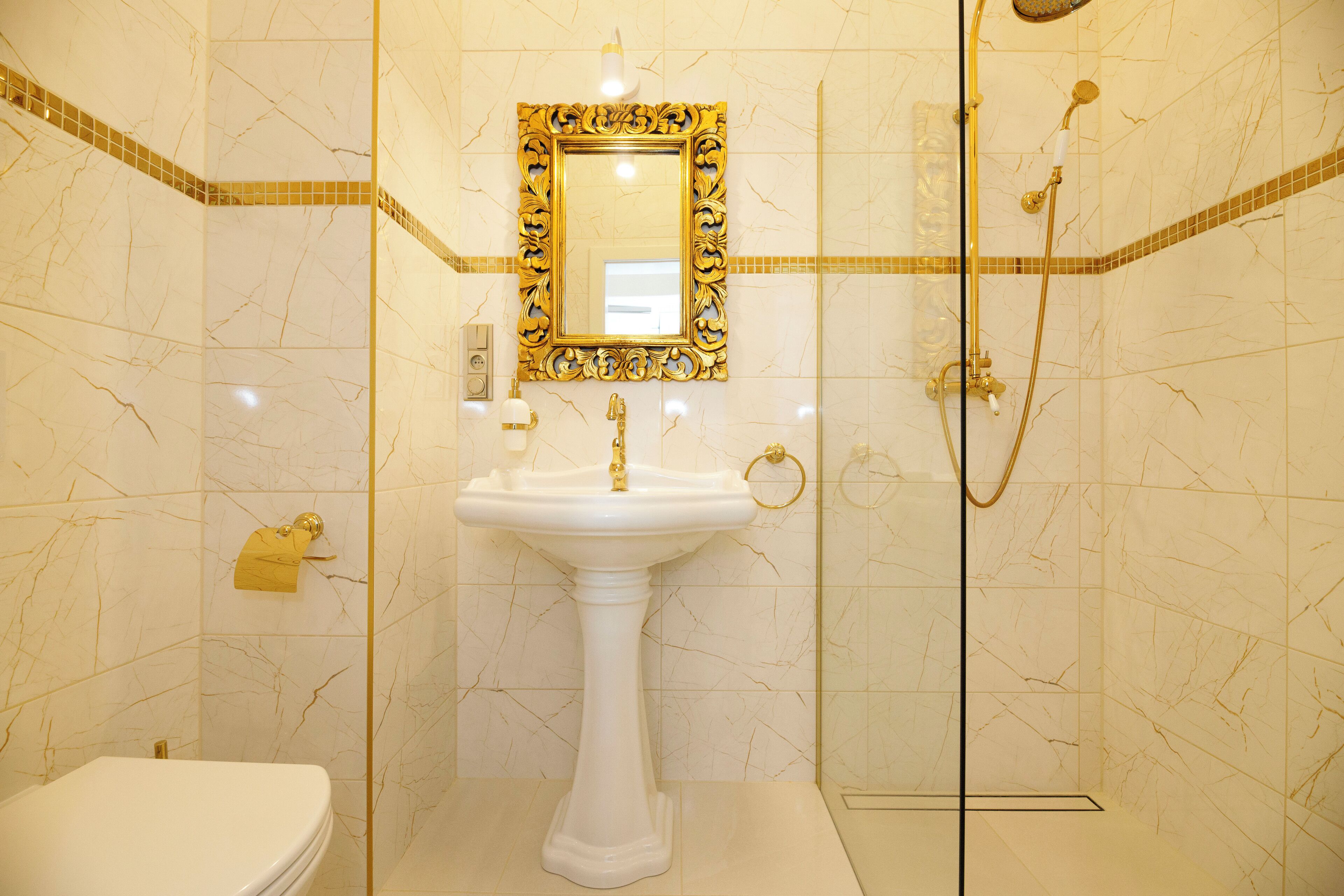 Une salle de bain avec un lavabo sur colonne, des toilettes, une douche et un miroir avec un cadre doré.