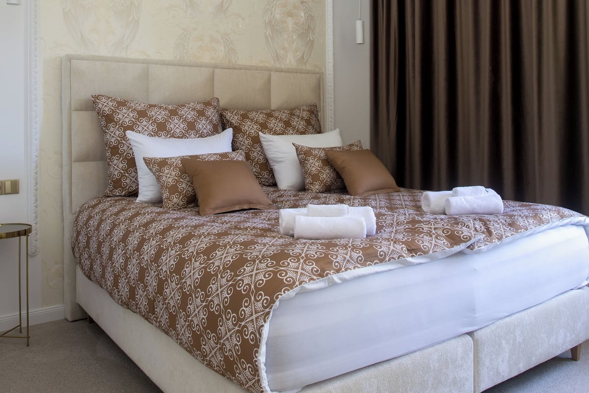 Een net opgemaakt bed met een bedsprei met dessin, een hoofdbord en een kroonluchter erboven.