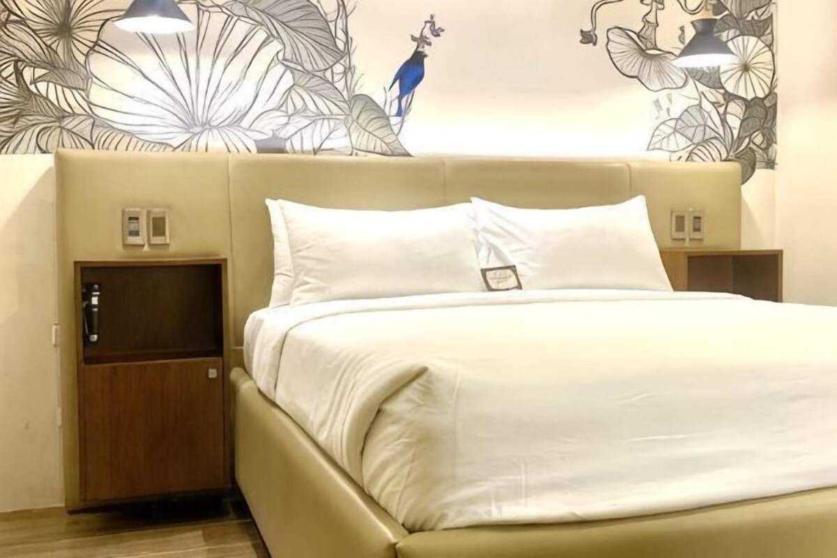 A hotel room with a bed, nightstands, and a wall with a floral pattern.