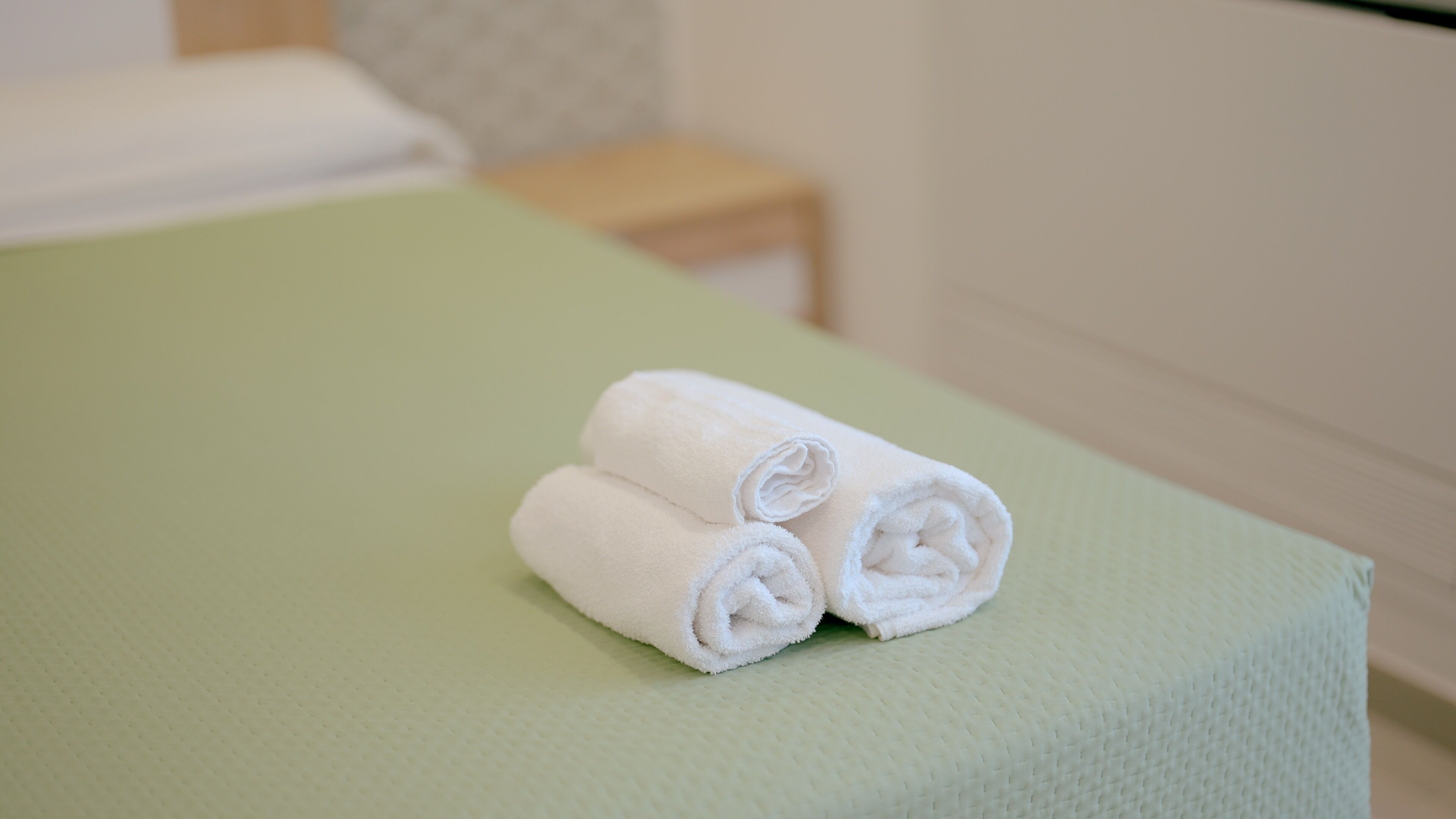 Letto rifatto con copripiumino verde e due asciugamani bianchi arrotolati sopra.