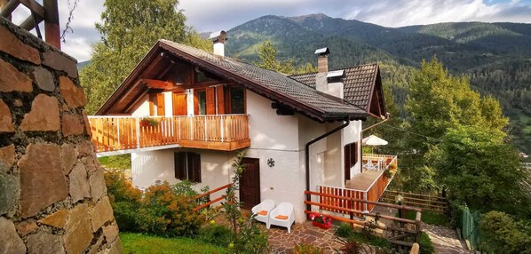 A two-story chalet with a balcony, stone walls, and a view of mountains. - Spacious apartment with balcony and terrace. Rural location with great views! (Dimaro)