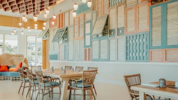 A dining area with wicker chairs and a wooden table, a wall with decorative shutters, and hanging pendant lights.